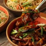 Close-up of glossy Indo-Chinese chilli chicken with onions, dried chillies and spring onions, served alongside vegetable noodles and fried rice at Food Exchange Aerocity Delhi
