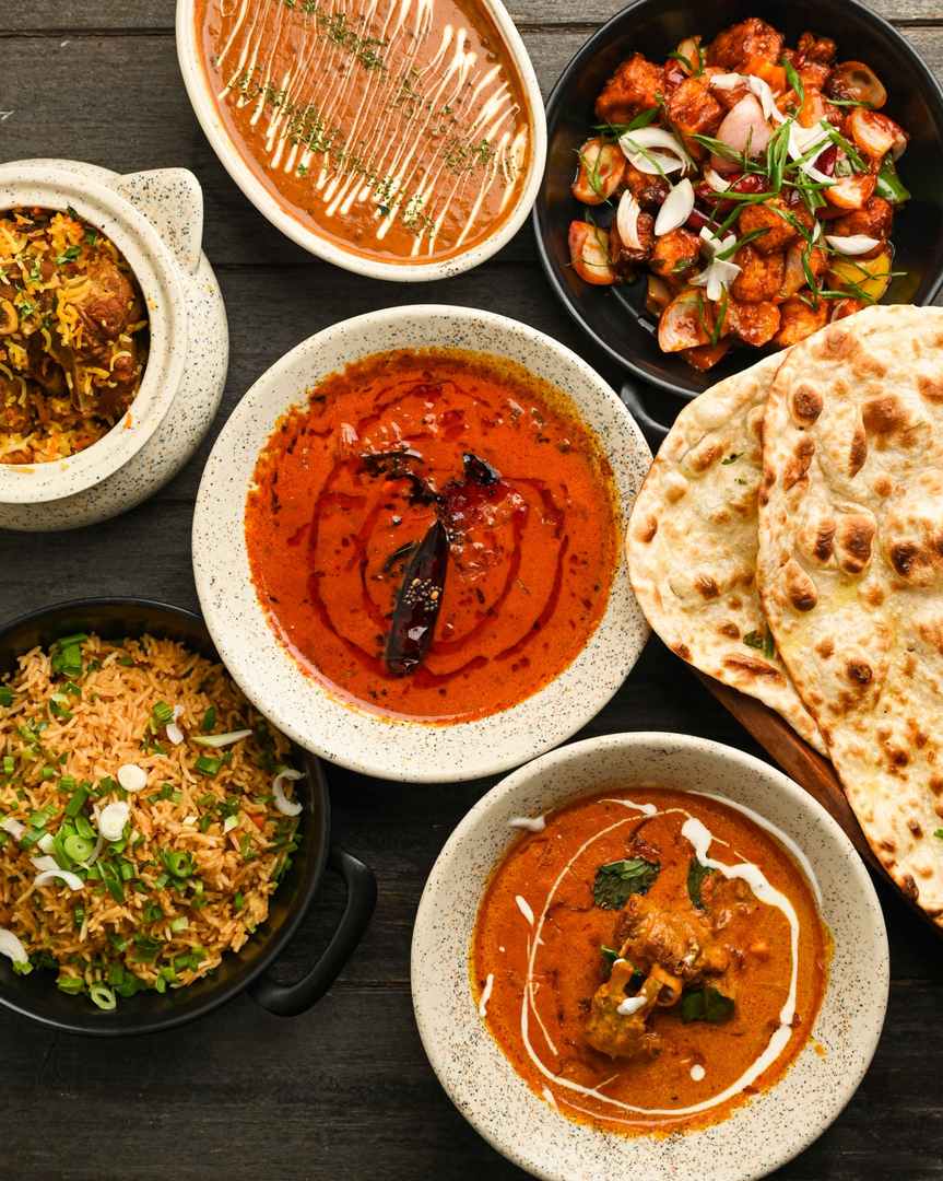 Overhead spread of Indian curries, biryani, fried rice, spicy paneer and freshly baked naan at Food Exchange Aerocity Delhi